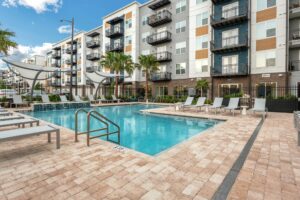 Modern apartment complex pool area with lounge chairs, palm trees, and contemporary shade structures.