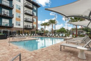 Modern apartment complex with pool, lounge chairs, and palm trees under a clear blue sky. Ideal for relaxation.