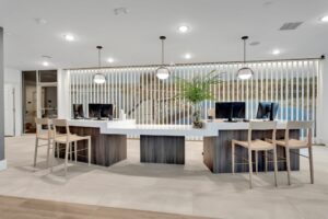 Modern reception area with computers, chairs, pendant lights, and potted plant, featuring elegant design elements.