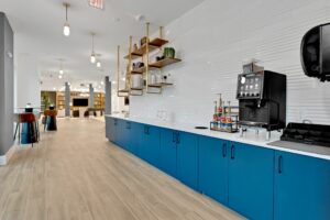 Modern office kitchen with blue cabinets, coffee machine, and stylish seating area.