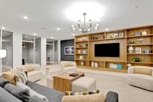 Modern lounge area with cozy seating, wooden shelves, and a large TV, featuring elegant lighting and decor.