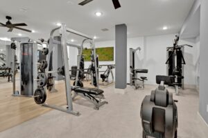 Modern gym with fitness machines, weights, and exercise equipment on light wood flooring.