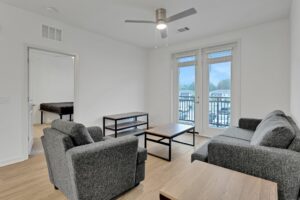 Modern living room with gray sofa set, wooden floor, and large windows opening to a balcony.