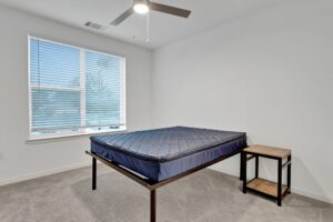 Minimalist bedroom with window blinds, ceiling fan, blue mattress on black frame, and wooden side table.