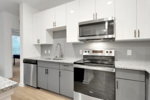 Modern kitchen with stainless steel appliances, granite countertops, and white cabinets, featuring a built-in microwave.