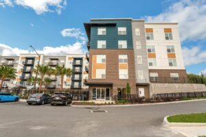 Modern apartment complex with blue sky and parked cars in front.