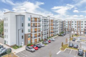 Modern apartment complex with balconies and parking lot, against blue sky. Urban living, residential architecture.