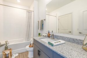 Modern bathroom with granite countertop, sink, mirror, and shower with white curtain.