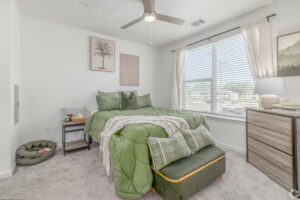 Cozy bedroom with green bedding, modern decor, large window, and ceiling fan, creating a bright and inviting space.