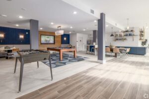Modern recreational room with foosball, pool table, and dining area, featuring chic lighting and seating.