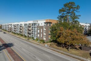 Modern apartment complex beside a major road under a clear blue sky.